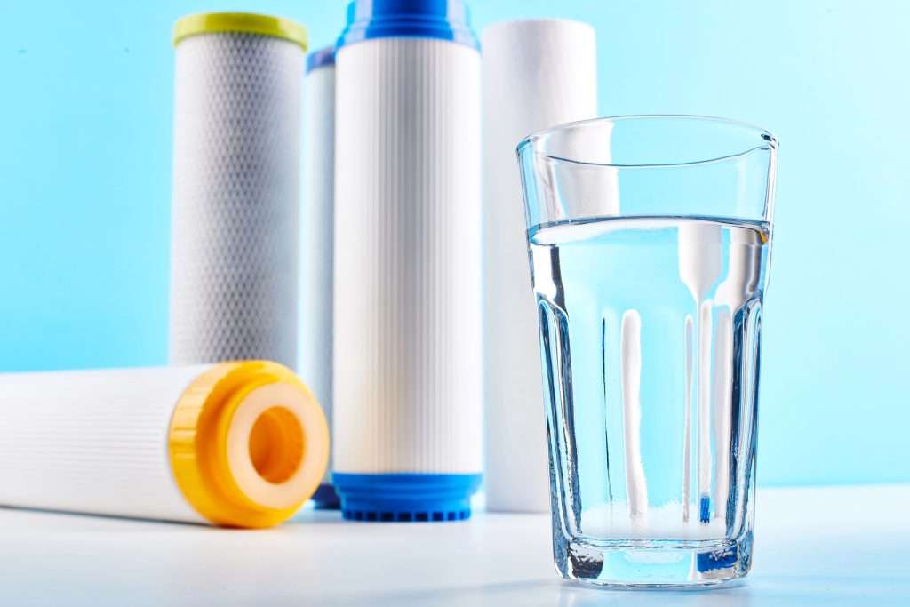 A clear glass of water resting on a white table with multiple water filters in the background.